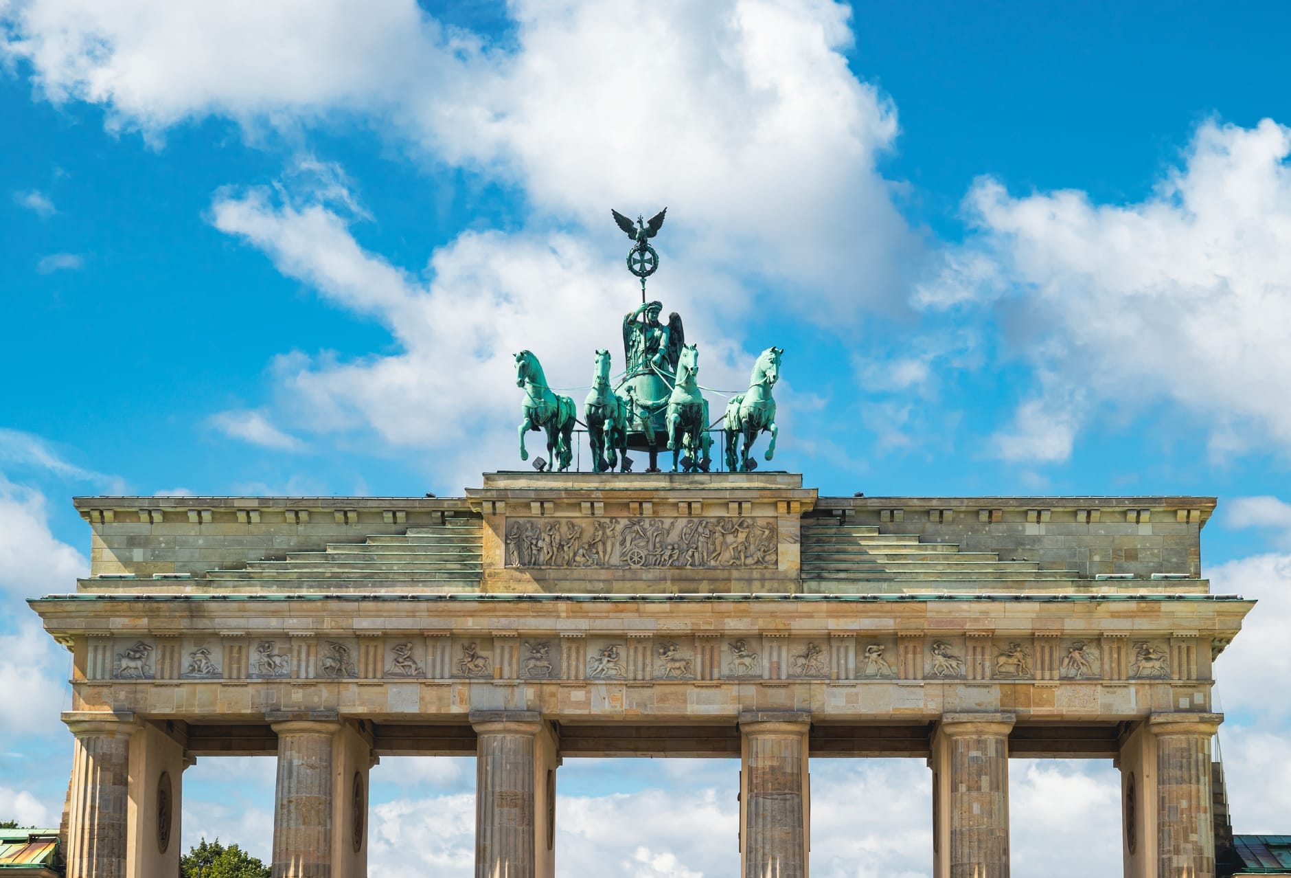 Vista grandangolare della Porta di Brandeburgo a Berlino sotto un cielo azzurro brillante con nuvole sparse, che mette in risalto le colonne del monumento e la statua della Quadriga.