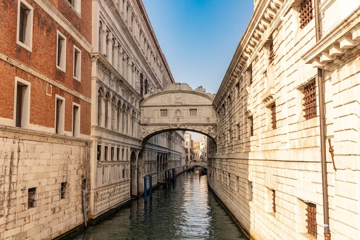 Die Seufzerbrücke in Venedig – eine überdachte Brücke aus weißem Kalkstein, die einen schmalen Kanal zwischen zwei historischen Gebäuden überspannt, mit Wasser darunter und blauem Himmel darüber.