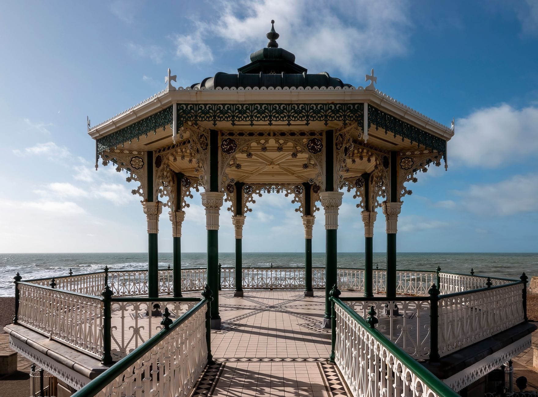 Brighton Bandstand viewed from the seafront promenade, showing ornate Victorian cast-iron structure with the English Channel in the background on a sunny day.