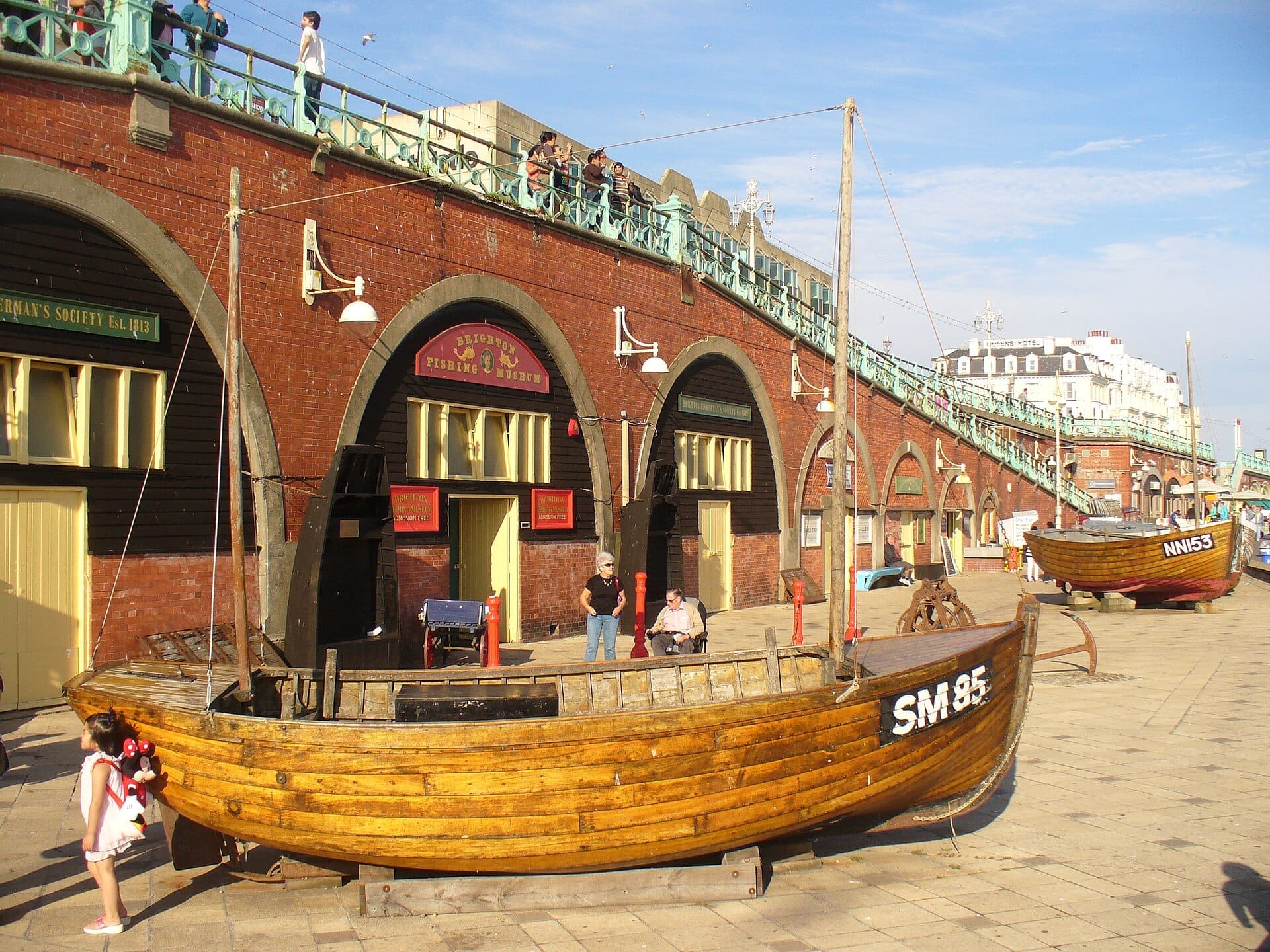 Exterior view of Brighton Fishing Museum with traditional wooden fishing boats displayed outside the historic brick arches on Brighton seafront.