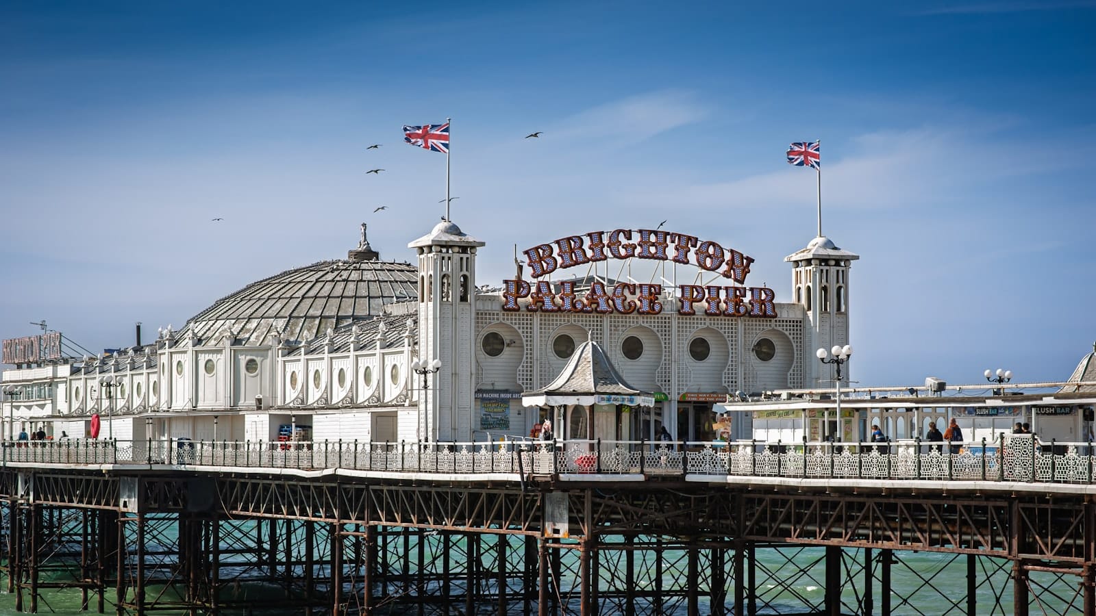 Brighton Palace Pier photographed from a distance with dramatic blue skies and seagulls, showcasing white Victorian architecture and the vibrant seaside atmosphere.