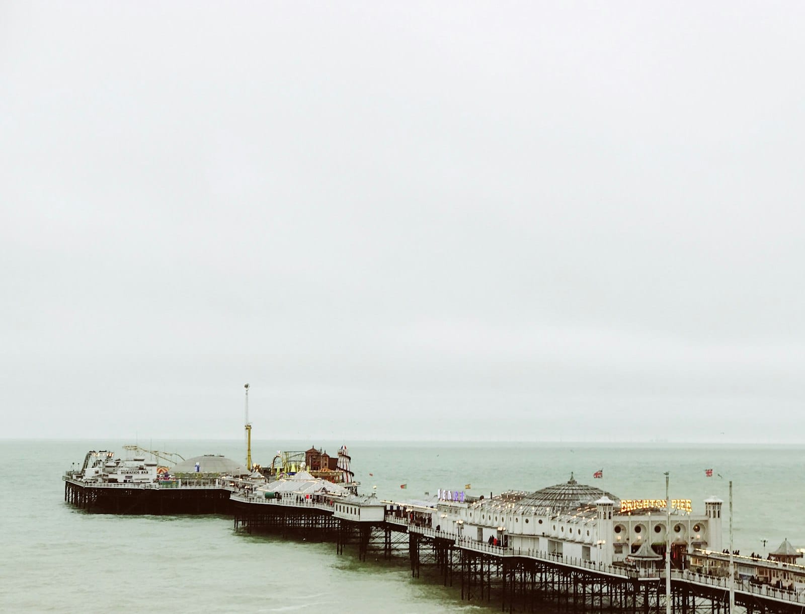 Bewölkter Winterhimmel über Brighton Palace Pier und dem Meer, mit gedämpften Farben und ruhigem Wasser, typisch für Winterwetter.