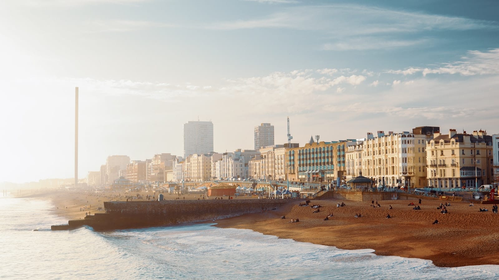 A wide landscape view of Brighton’s beachfront with the iconic i360 tower, historic buildings, and a quiet, golden winter light over the shore.