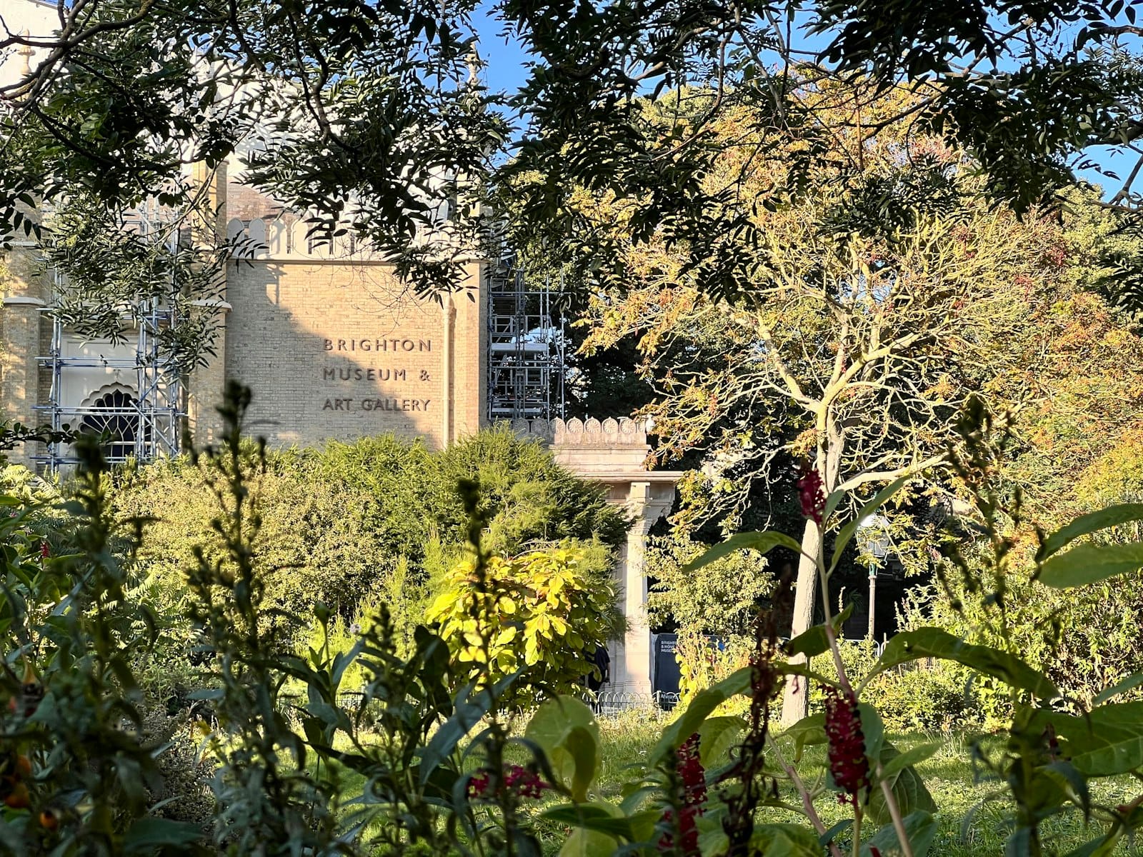 Widok na Brighton Museum & Art Gallery przez ogrodową roślinność i drzewa w słoneczny dzień