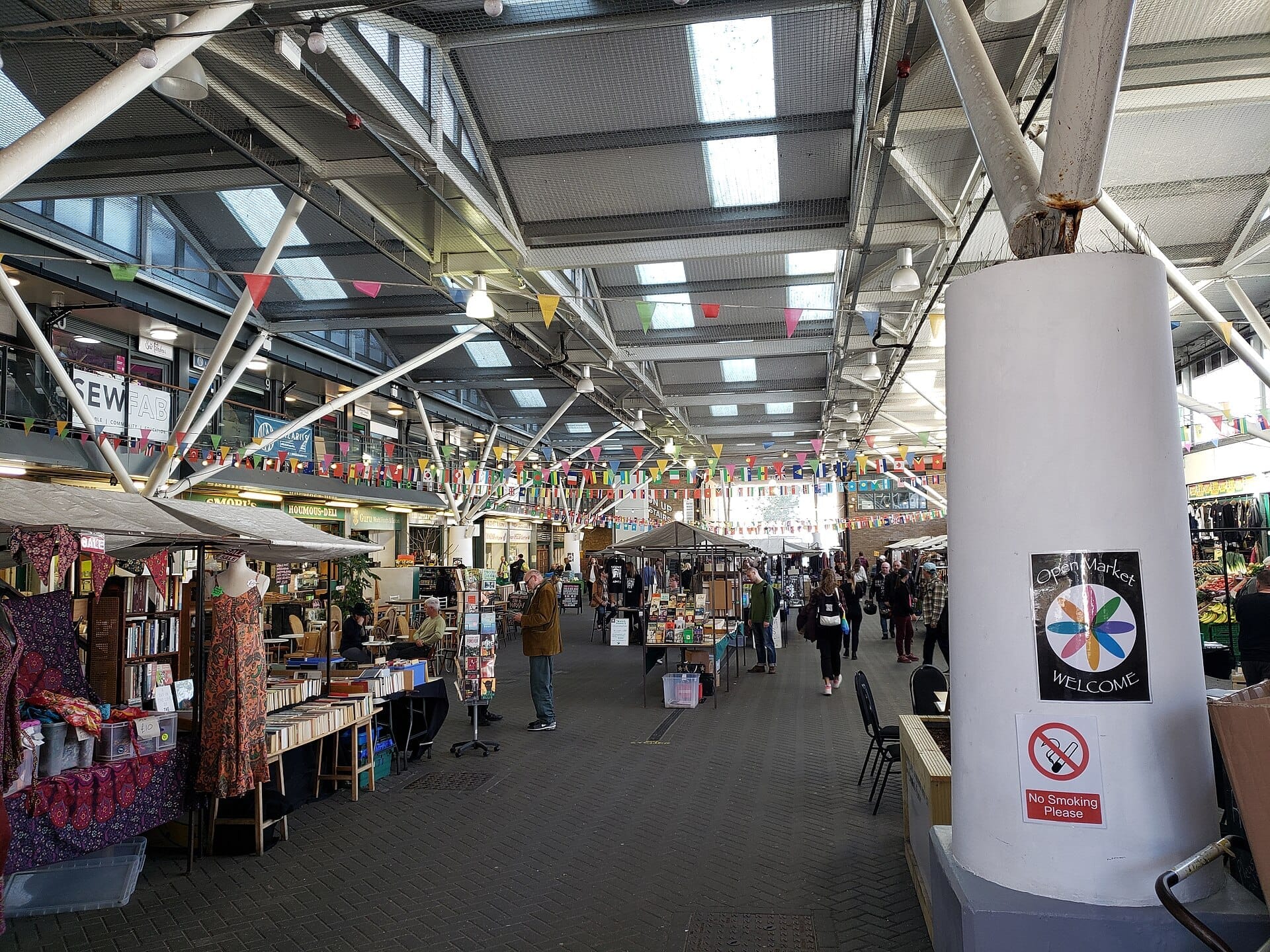 Brighton Open Market with covered roof, colorful bunting, independent stalls, shoppers browsing books, and handmade goods in a vibrant indoor setting.