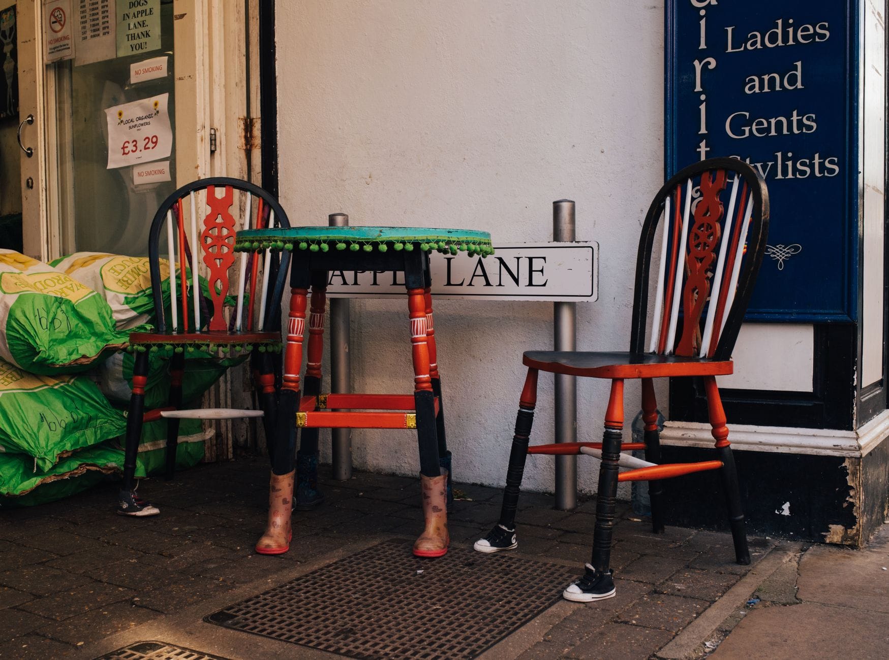 Escena callejera de Brighton con sillas pintadas de colores y una mesa en una estrecha acera, con un letrero frente a una tienda en the Lanes.
