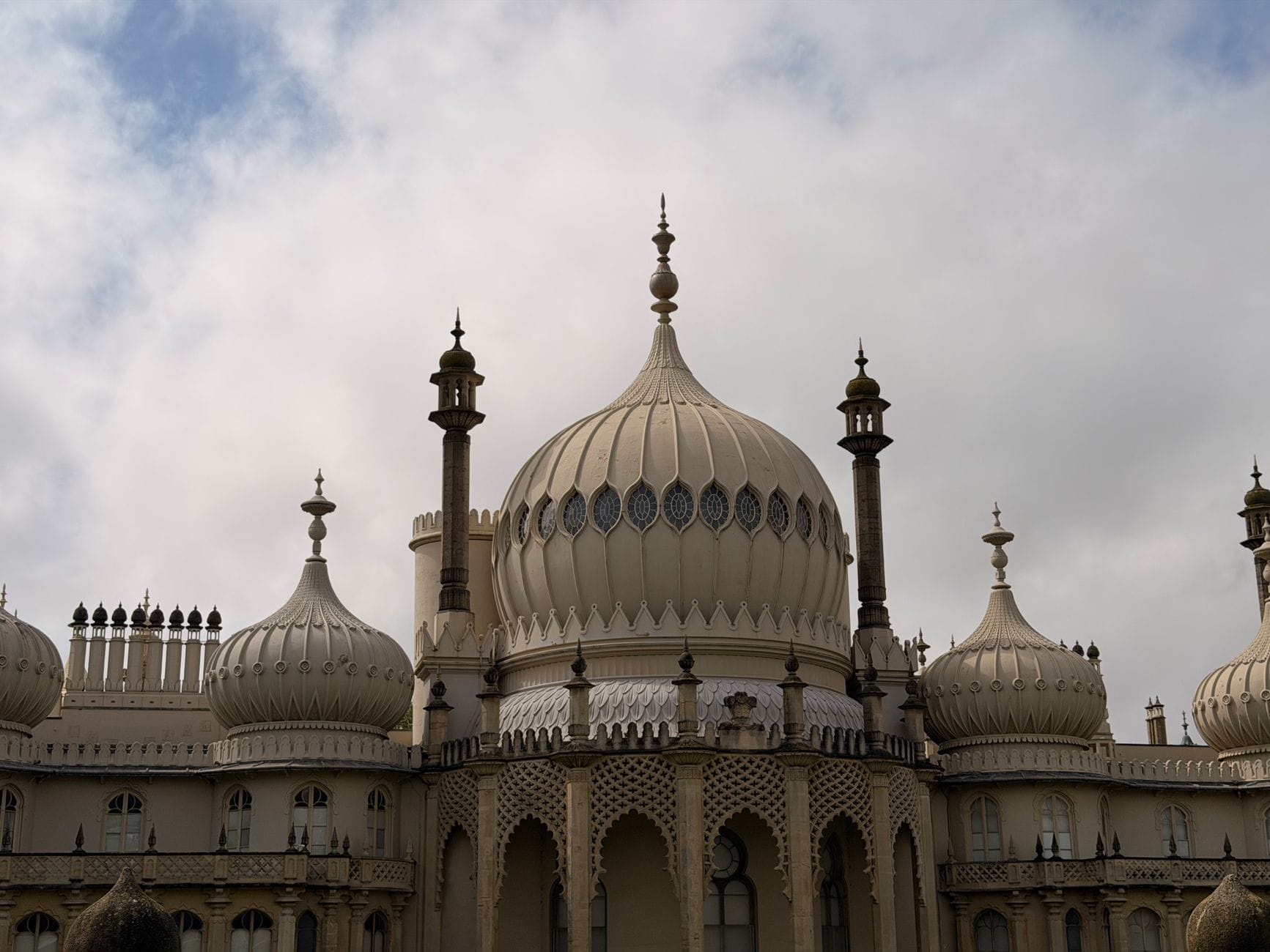Nahaufnahme der verzierten Kuppeln und Minarette des Royal Pavilion vor einem bewölkten Himmel in Brighton.