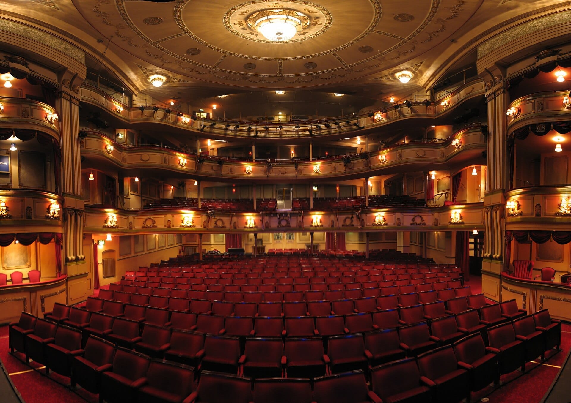 View of Theatre Royal Brighton's ornate Regency auditorium with red velvet seats, balcony tiers, and elegant chandeliers under warm lighting.