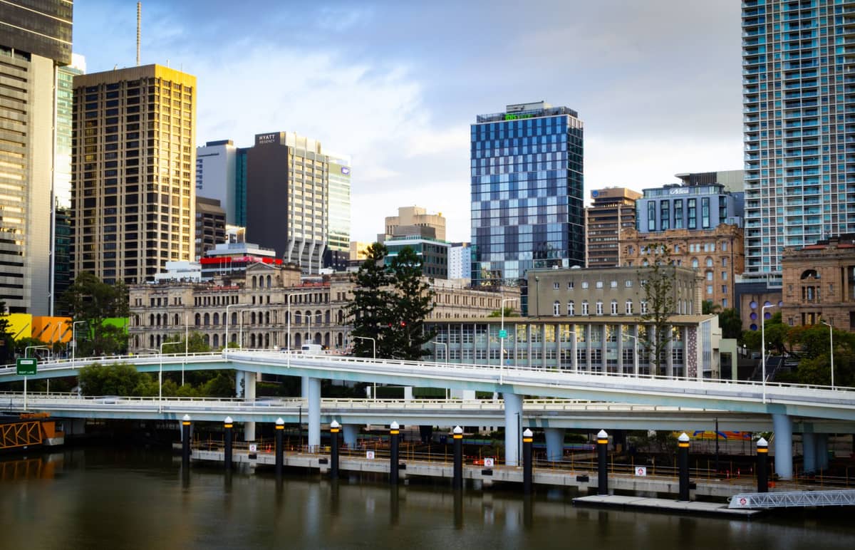 Panorama Brisbane z widocznymi zabytkowymi budynkami wzdłuż nabrzeża – XIX-wieczne kamienne konstrukcje i nowoczesne wieżowce w tle.