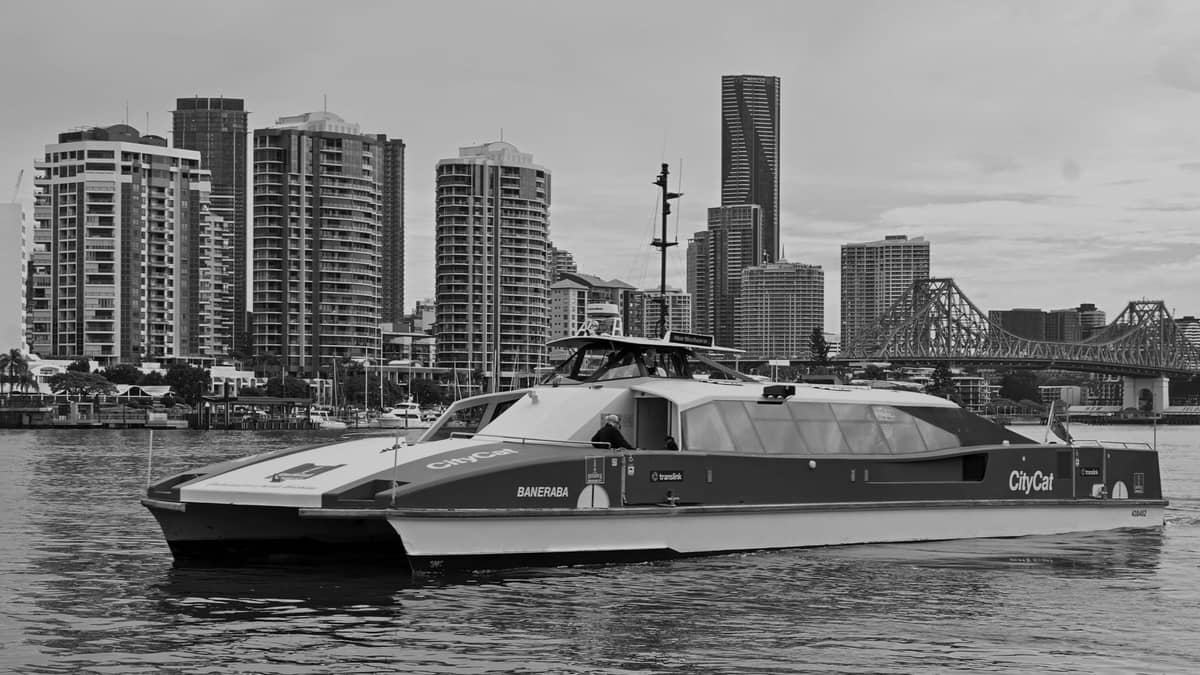Un ferry de pasajeros CityCat de Brisbane en el río con el horizonte de la ciudad y el Story Bridge al fondo.