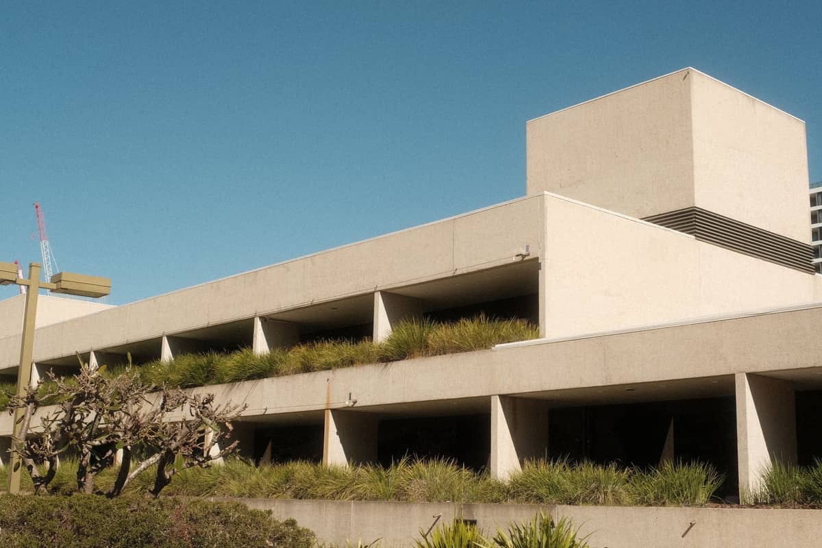Exterior of a modern concrete building with layered architecture and native landscaping, photographed under a clear blue sky.