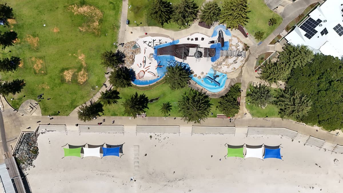 Vista aérea de South Bank Parklands con área de juegos, césped verde, carpas de sombra y una zona de playa de arena en Brisbane.