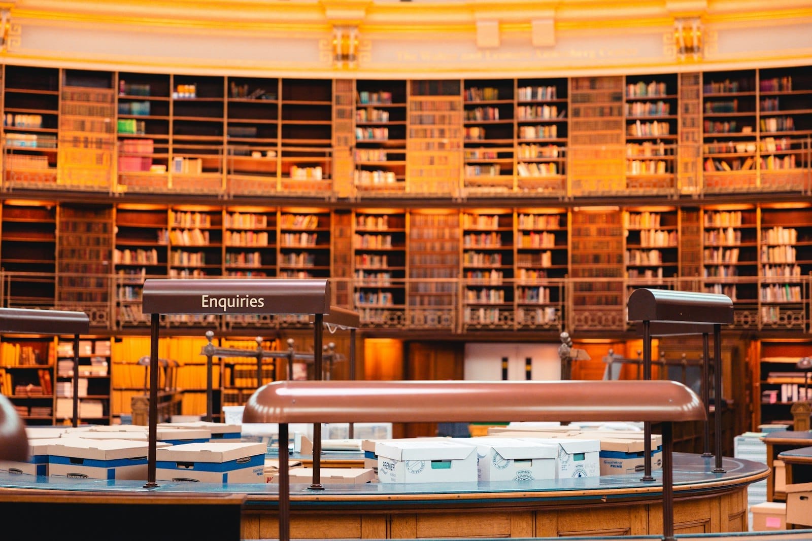 File di scaffali e un banco informazioni all'interno della grande sala di lettura della British Library, illuminata con caldi toni dorati.