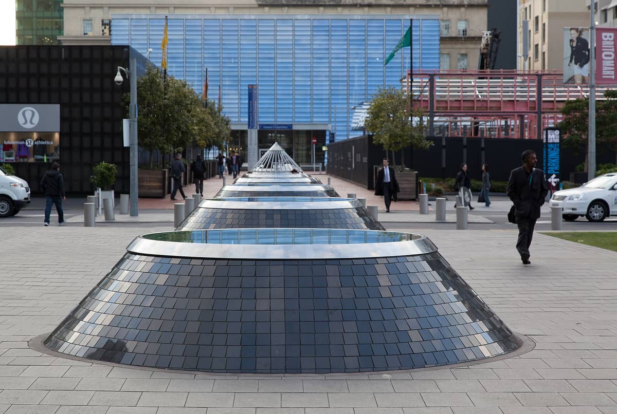 บรรยากาศกลางวันย่าน Britomart ในโอ๊คแลนด์ โดดเด่นด้วยหลังคาแก้วพีระมิดกลางจัตุรัส ผู้คนเดินผ่านไปร้านค้าสมัยใหม่โดยรอบ