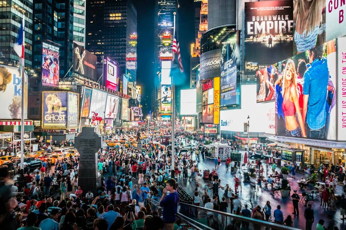 Belebter Times Square mit Menschenmassen, hellen Lichtern und Taxis in Midtown Manhattan bei Nacht.