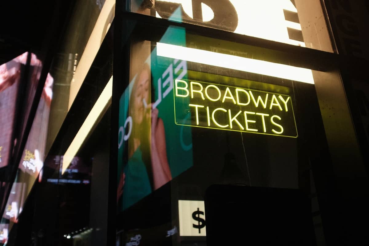 Neonschild in einem Schaufenster mit der Aufschrift 'Broadway Tickets' mit Stadtlichtern und Reflexionen, das auf eine offizielle Ticketverkaufsstelle in New York City hinweist.