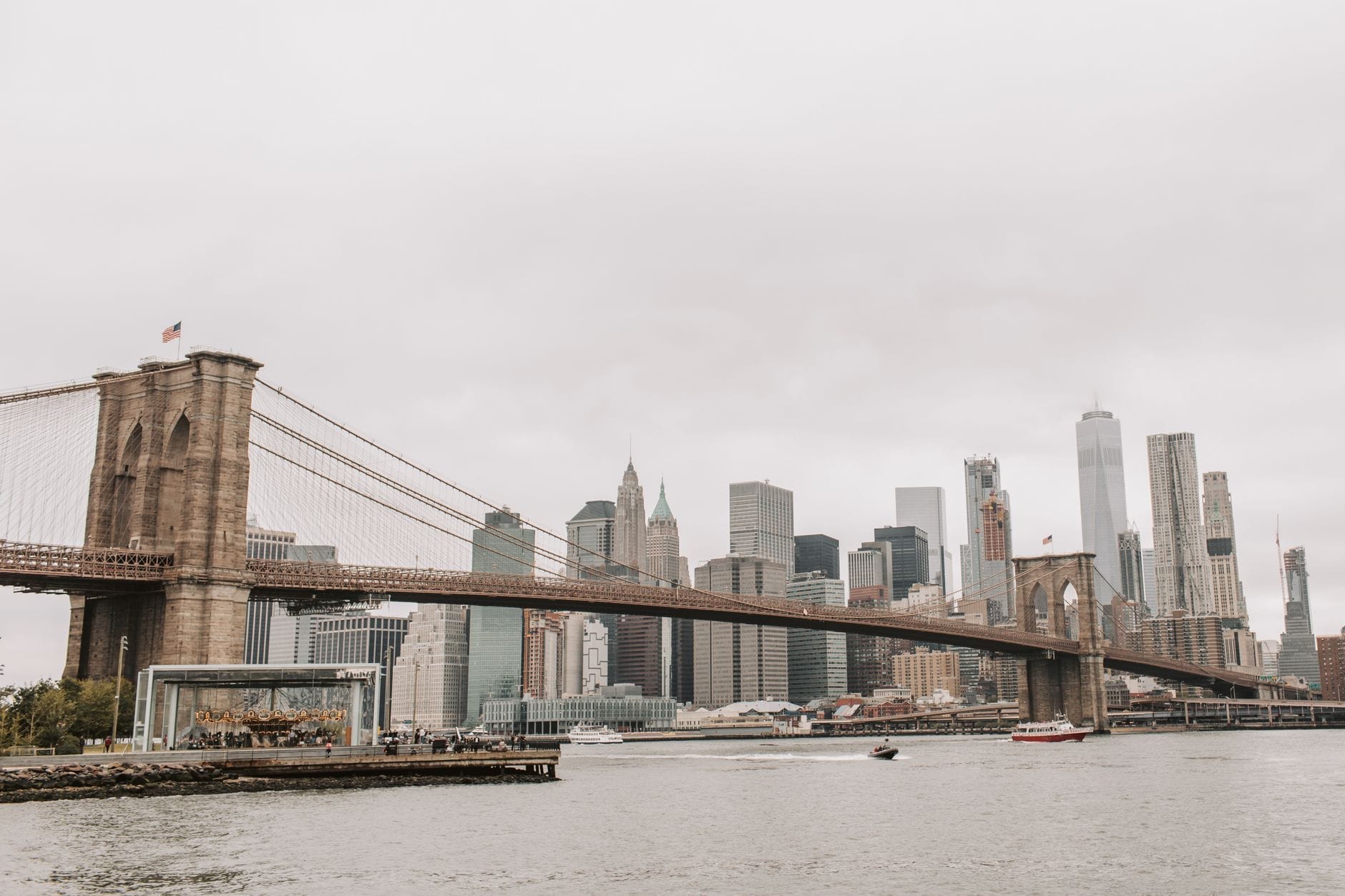 Ampia veduta panoramica del Ponte di Brooklyn che attraversa l'East River con lo skyline di Manhattan sullo sfondo in una giornata nuvolosa.