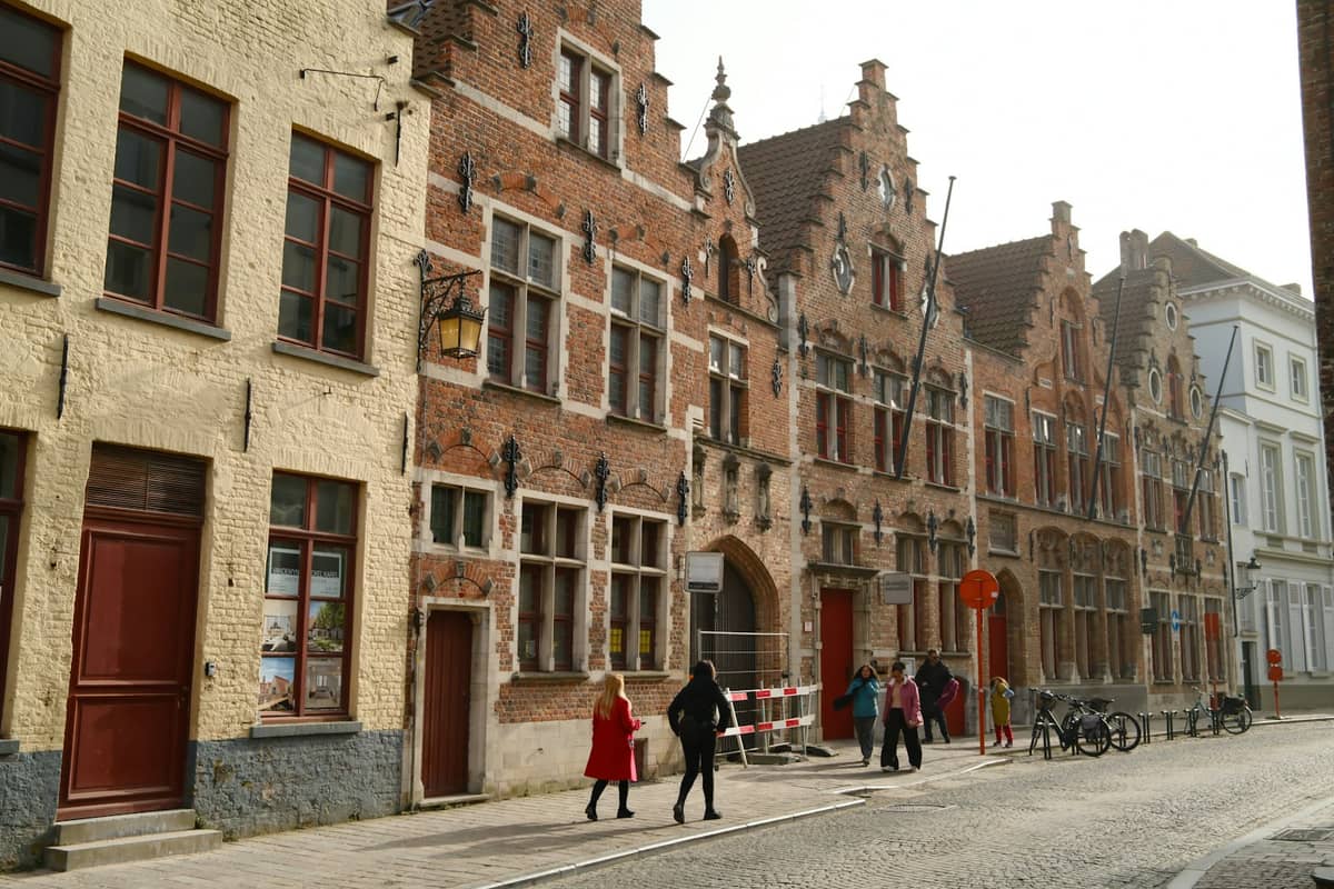 People walking along a cobblestone street lined with historic brick buildings in Bruges.