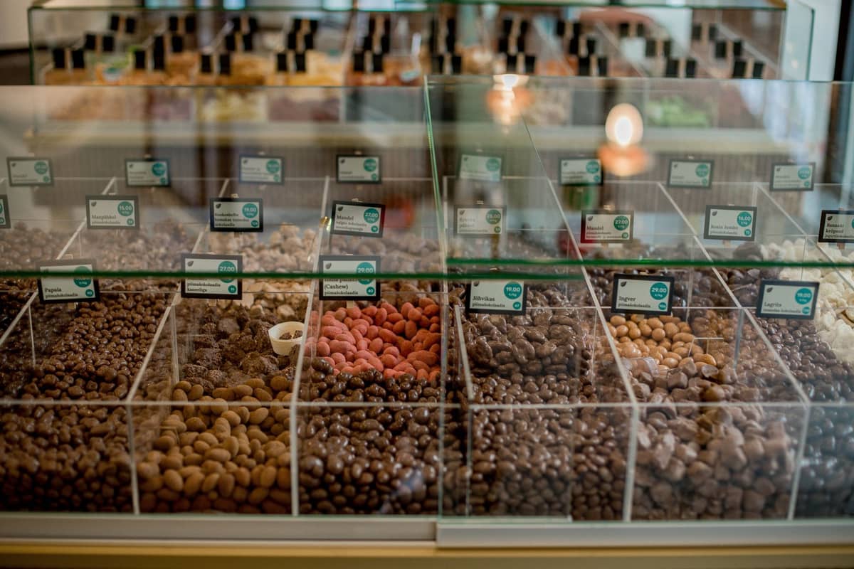 Glass display filled with various types of chocolate and confections in a shop, organized in clear bins with small labels.