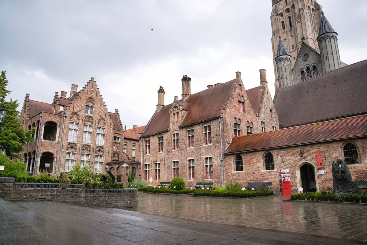 Landscape view of Bruges with prominent Gothic buildings and the Church of Our Lady tower under a cloudy sky.