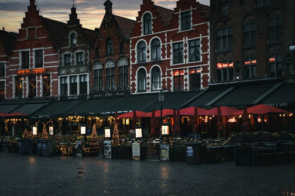 Cafe terraces with twinkling winter lights under Bruges’ iconic gabled buildings at dusk, evoking a cozy food and drink scene.
