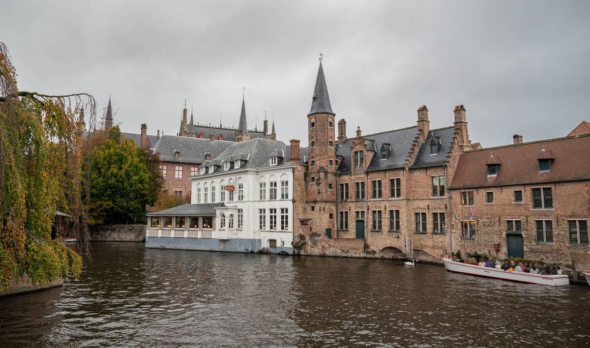 Overcast winter day in Bruges with bare trees, historic canalside brick buildings, and boats on the water.