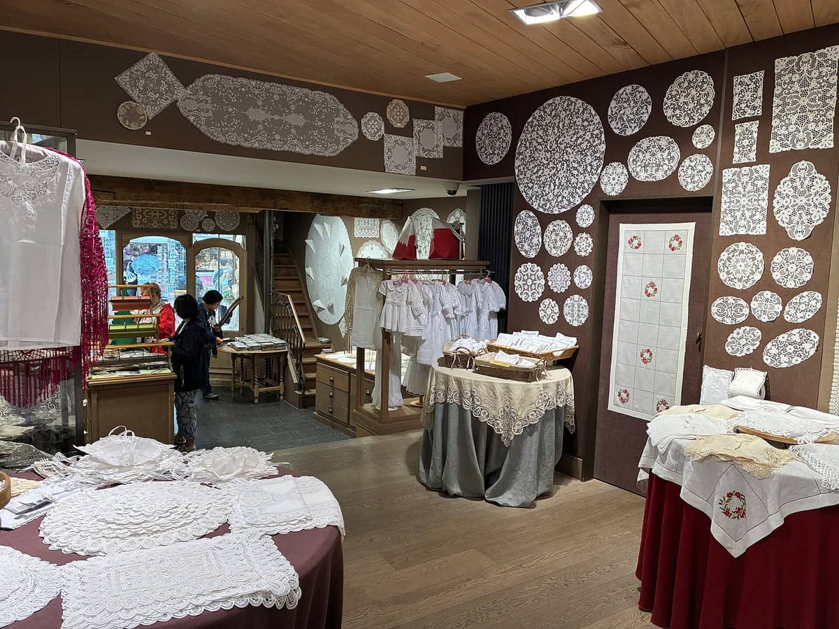 Interior of a Bruges lace shop with intricate handmade lace displayed on tables and walls, wooden floors, and warm lighting.