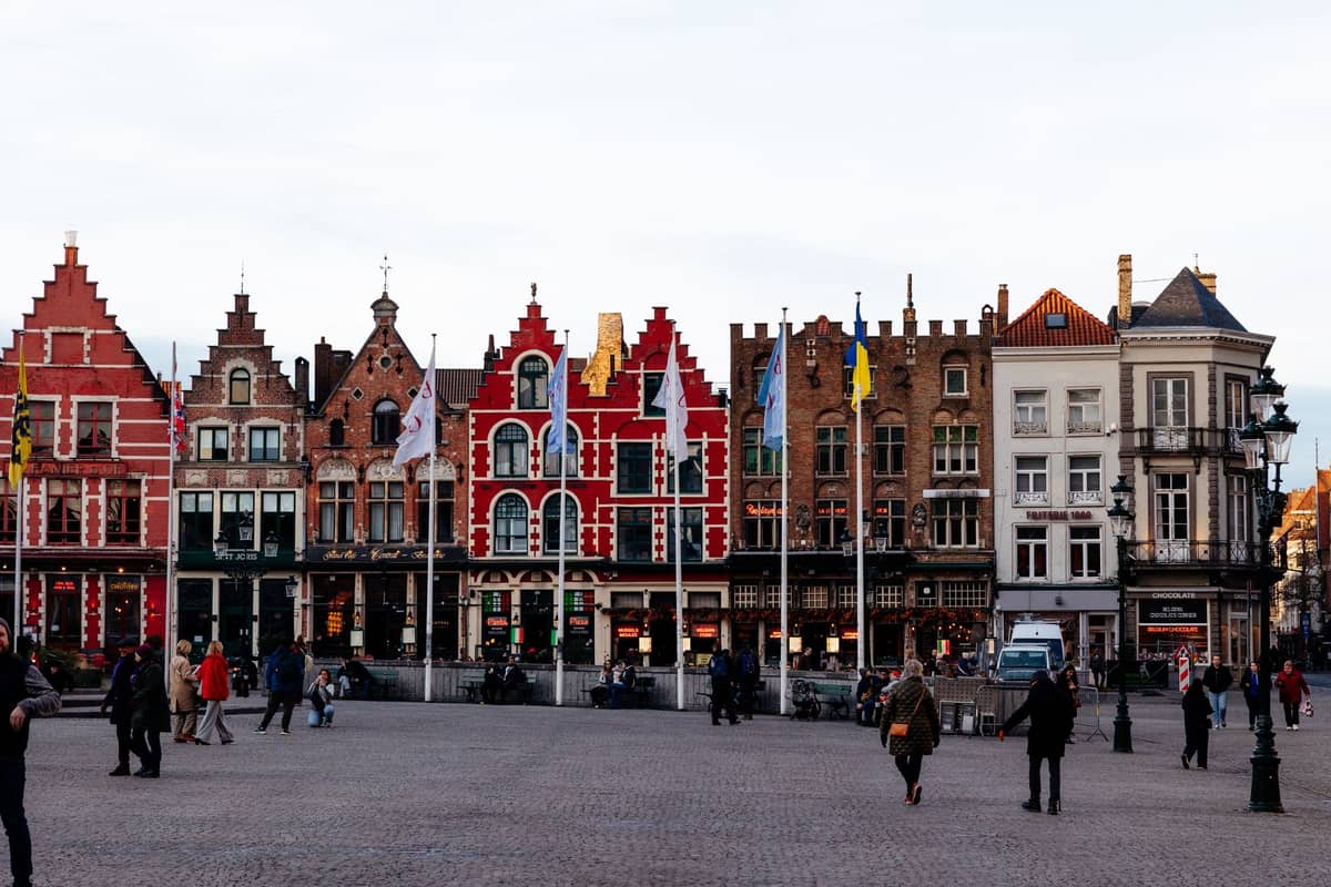 Bruges Markt Square with people walking, colorful stepped-gable buildings and flags, illustrating accessibility of main attractions on foot.