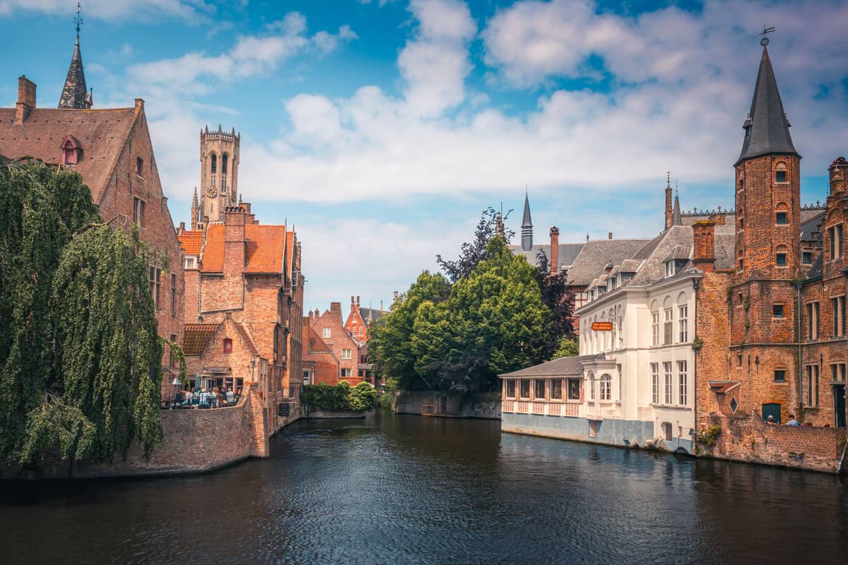 Picturesque canal in Bruges lined with medieval buildings and a stone bridge, inviting pedestrians to explore the historic city for free.