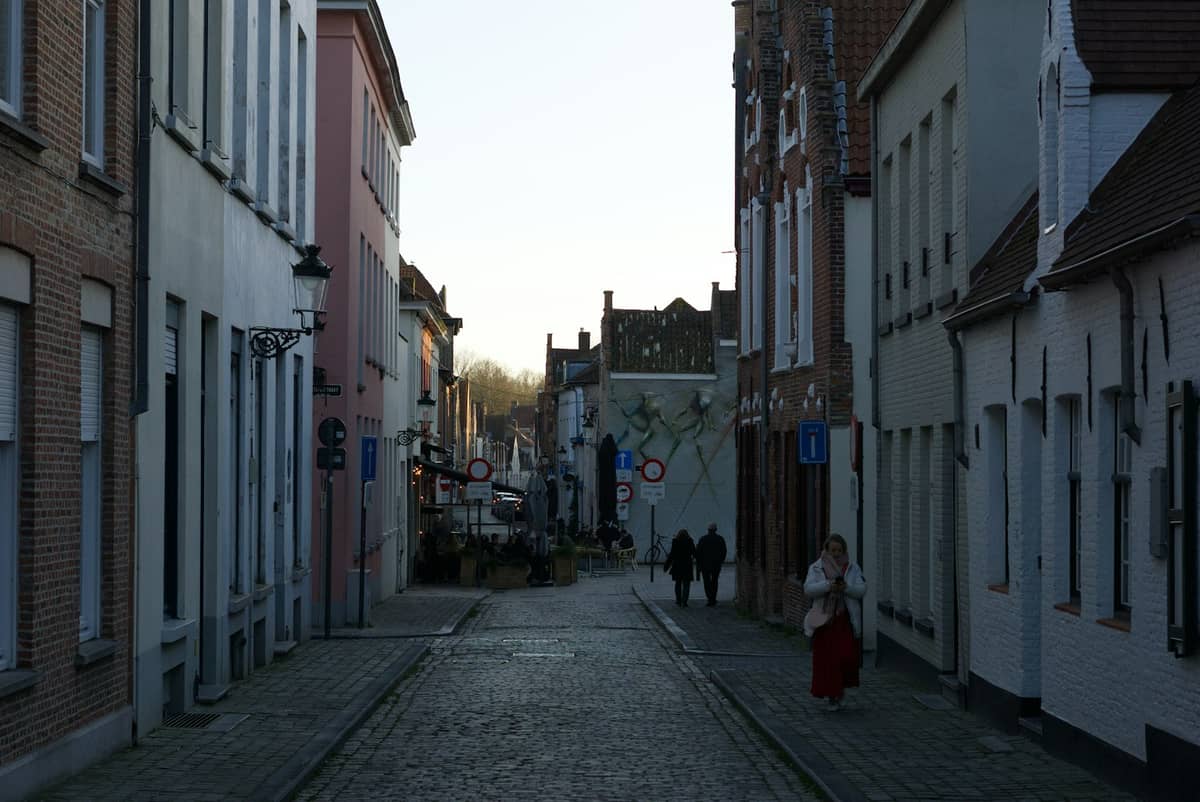 Quiet cobbled street in Bruges lined with traditional buildings and a few pedestrians in the distance.