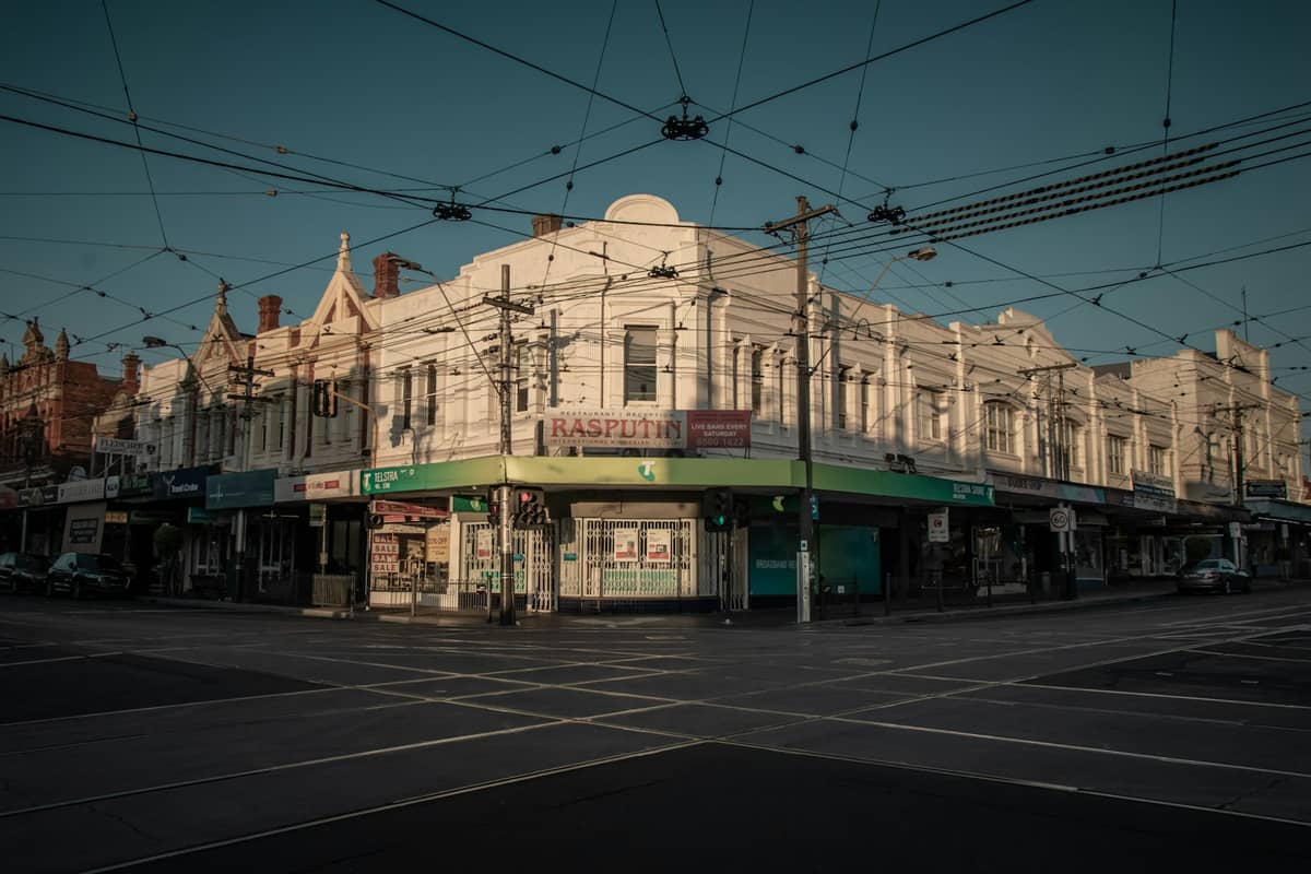หัวมุมถนนใน Brunswick ที่มีร้านค้าสไตล์เฮอริเทจ สายไฟรถรางเหนือศีรษะ และป้ายซุปเปอร์มาร์เก็ต Rasputin สะท้อนกลิ่นอายย่านตอนเหนือชั้นในของเมลเบิร์น
