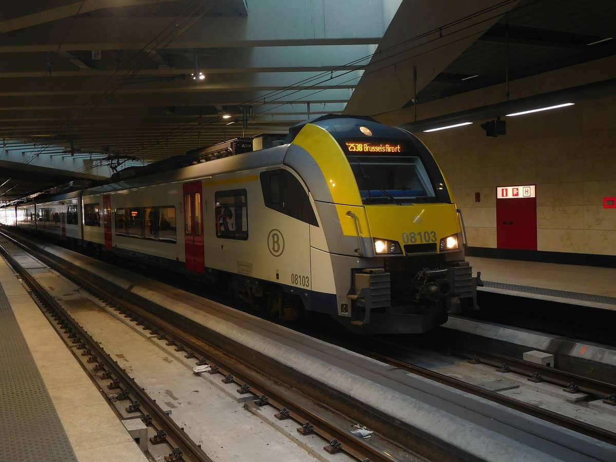 Trem com a indicação 'Brussels Airport' numa plataforma de estação subterrânea, mostrando a principal rota da SNCB de Brussels Airport ao centro da cidade.