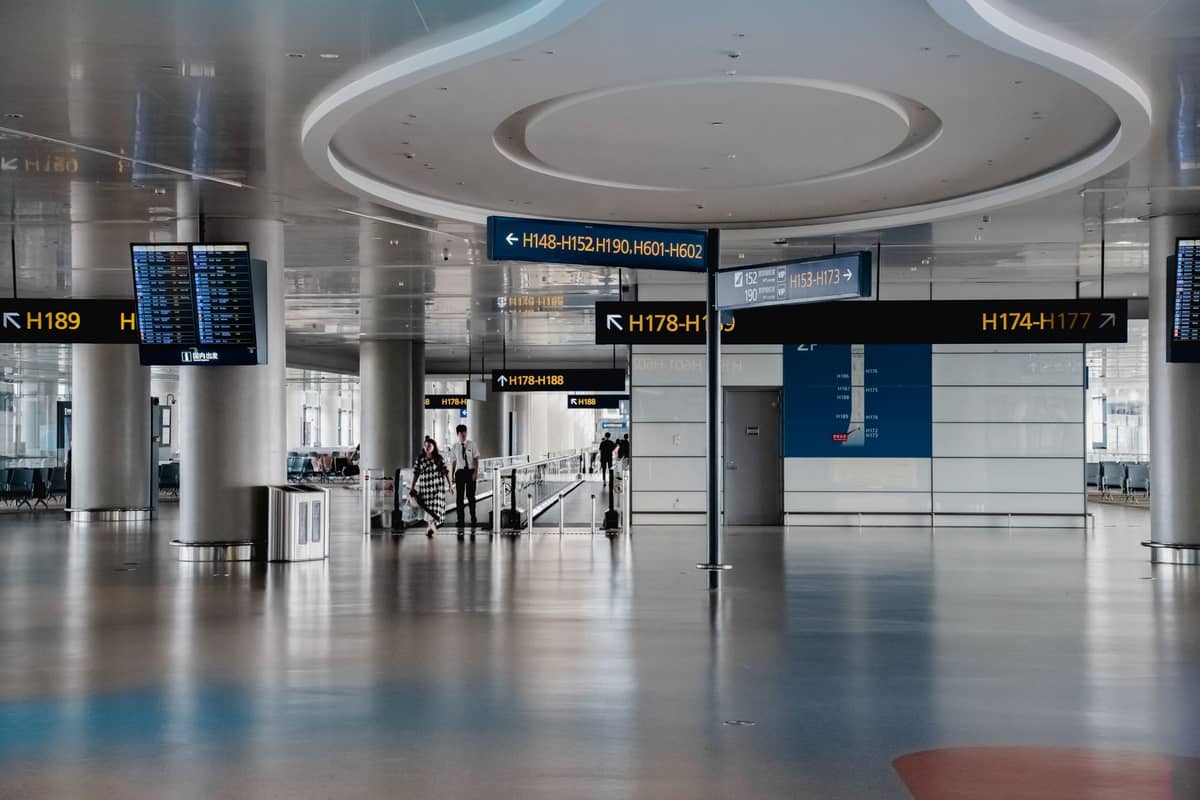 Vista ampla do interior de um terminal de aeroporto moderno com sinalizações no teto indicando números de portões e painéis digitais de informações de voo.