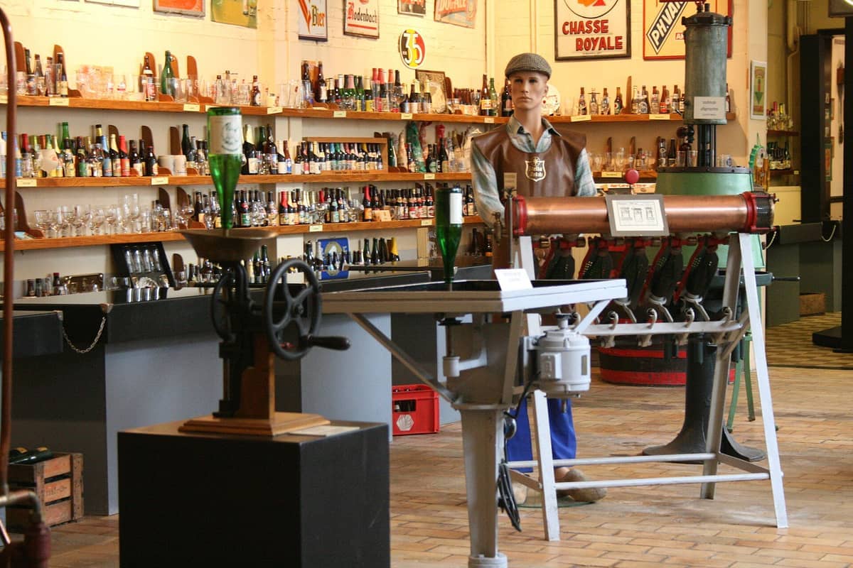 Prateleiras com garrafas e copos de cerveja belga, equipamentos antigos de fabricação de cerveja e um manequim com roupa de cervejeiro no Museu dos Cervejeiros Belgas.