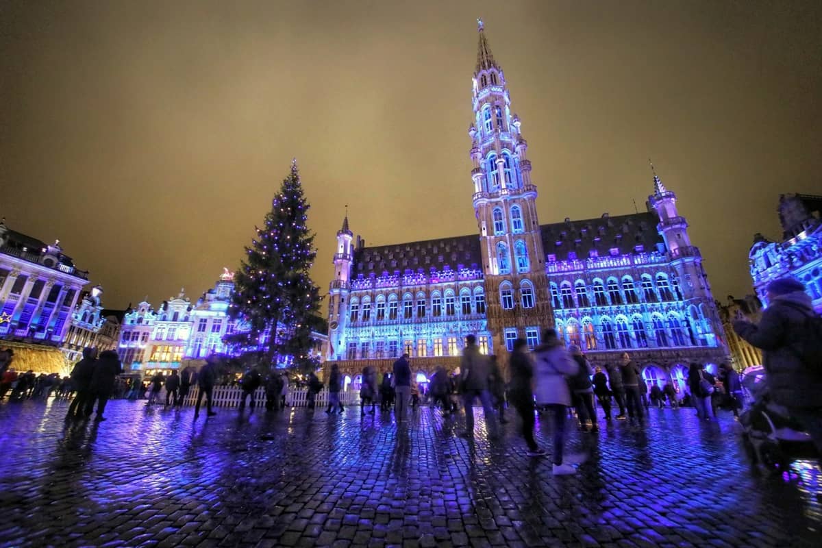 A Grand-Place de Bruxelas iluminada com luzes azuis e roxas e uma grande árvore de Natal durante o mercado de Natal Winter Wonders à noite.