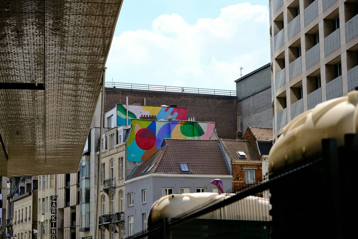 Um colorido mural de quadrinhos pintado numa parede alta em Bruxelas, cercado pela arquitetura típica da cidade sob um céu parcialmente nublado.