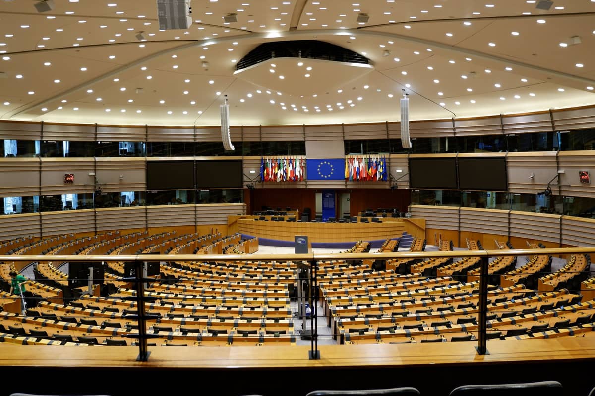 Vista ampla do hemiciclo do Parlamento Europeu em Bruxelas com assentos curvos, mesas e bandeiras da UE na frente.