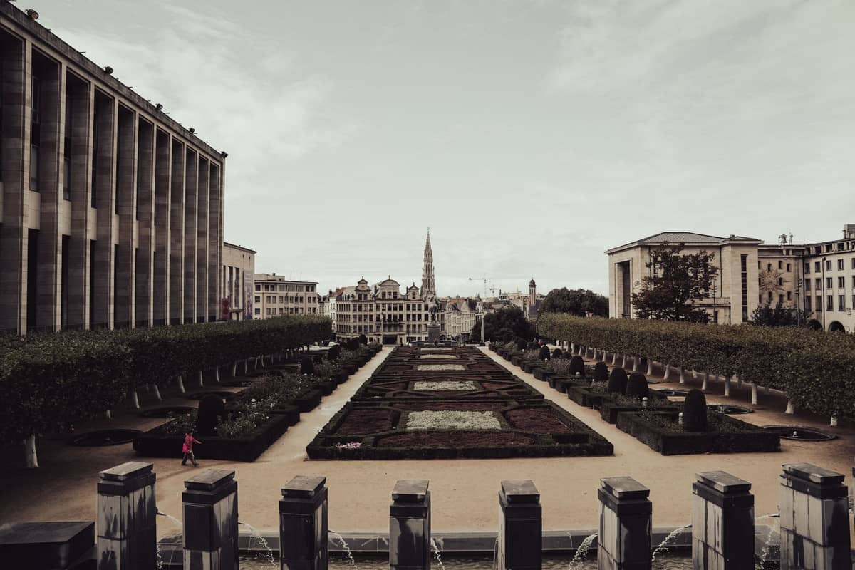 Vista ampla dos Jardins do Mont des Arts no centro de Bruxelas, com sebes bem aparadas, o horizonte da cidade e a torre da Câmara Municipal ao fundo.