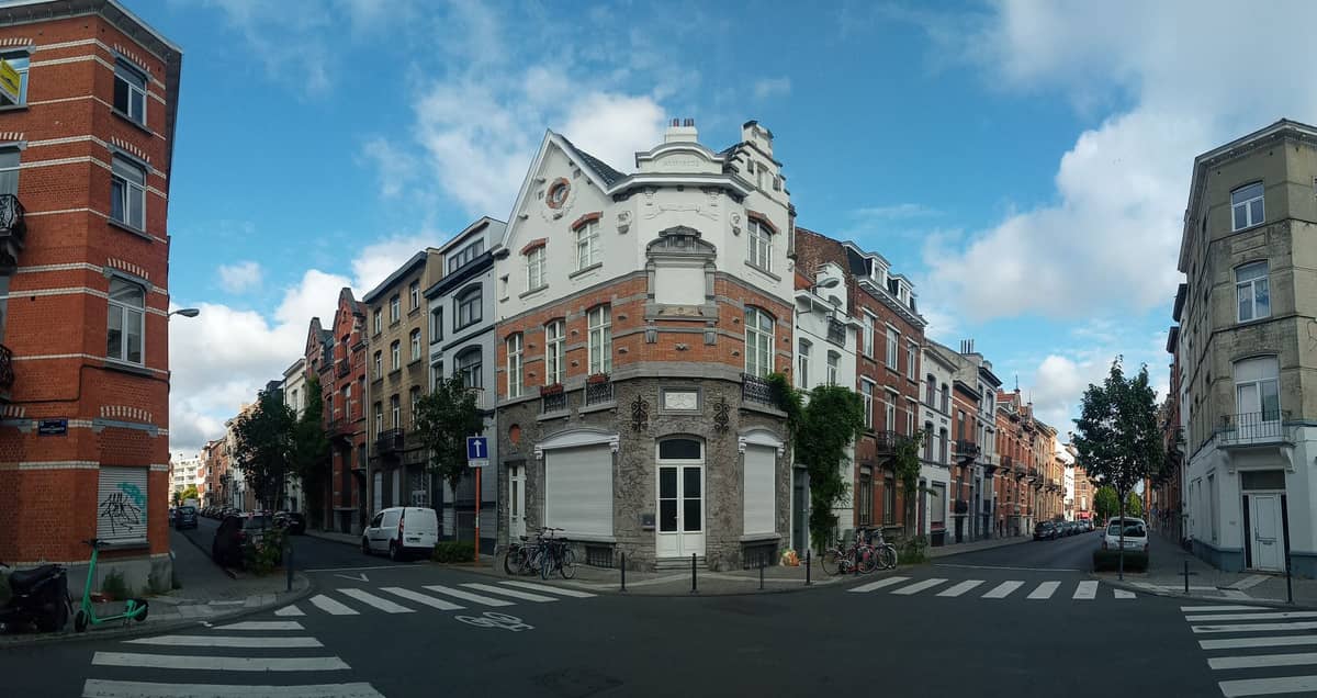 Bairro residencial típico de Bruxelas com ruas que se cruzam, casas geminadas de tijolos vermelhos e brancos, e bicicletas estacionadas sob um céu parcialmente nublado.