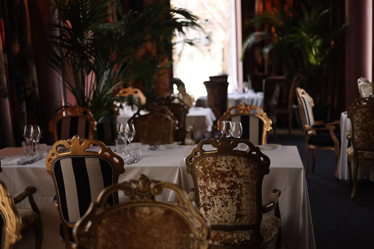 Sala de jantar opulenta com cadeiras de veludo, toalhas de mesa brancas e cristalaria, evocando o ambiente de um restaurante de alta gastronomia em Bruxelas.