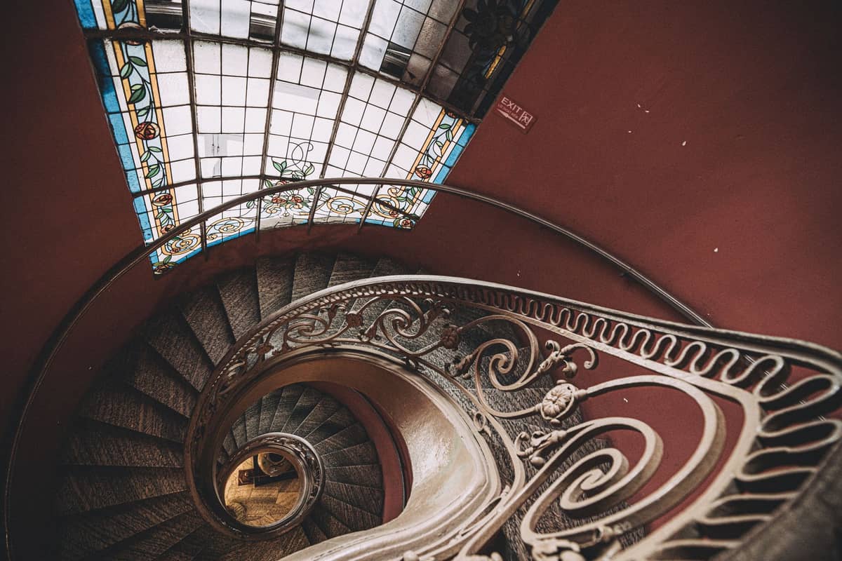 Escadaria em espiral com corrimão de ferro Art Nouveau ornamentado e vitral acima, vista de cima