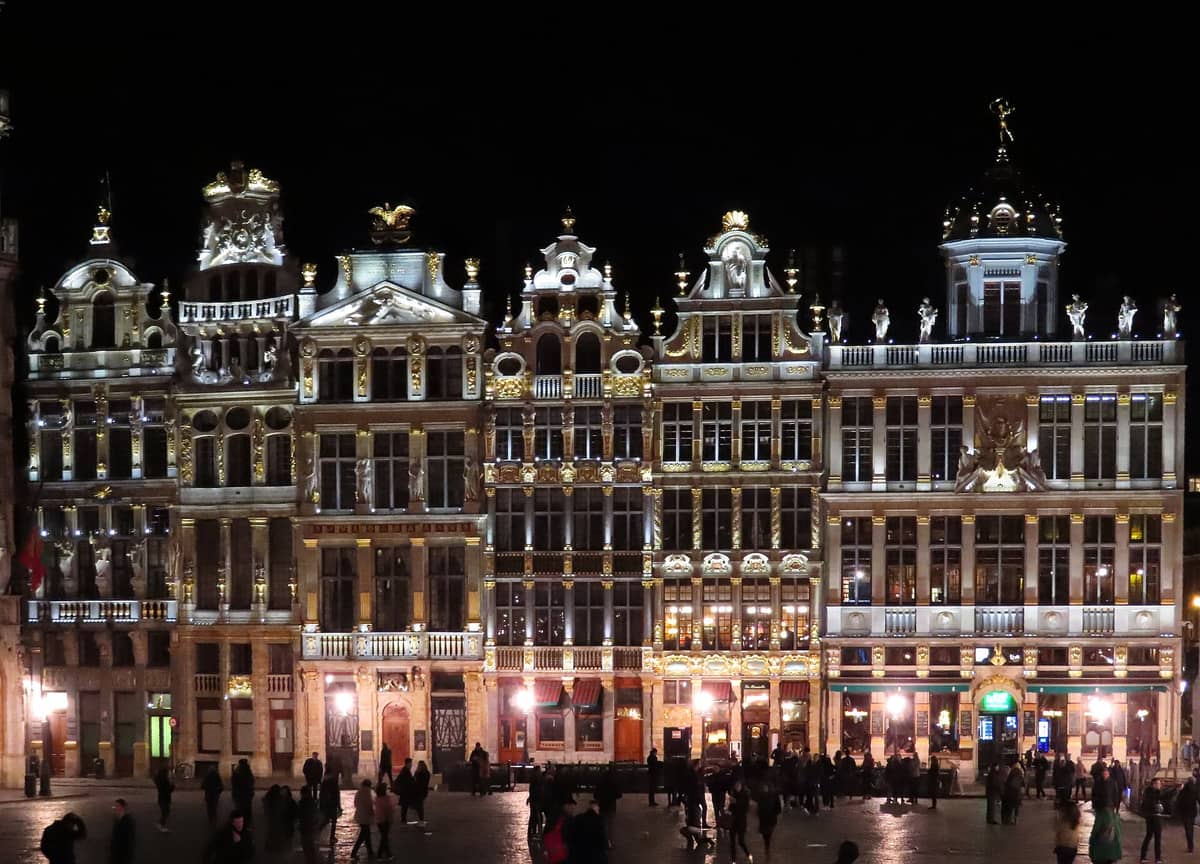 Vista noturna da Grand Place de Bruxelas, com ornamentadas casas de guilda iluminadas e pessoas caminhando pela praça de paralelepípedos.