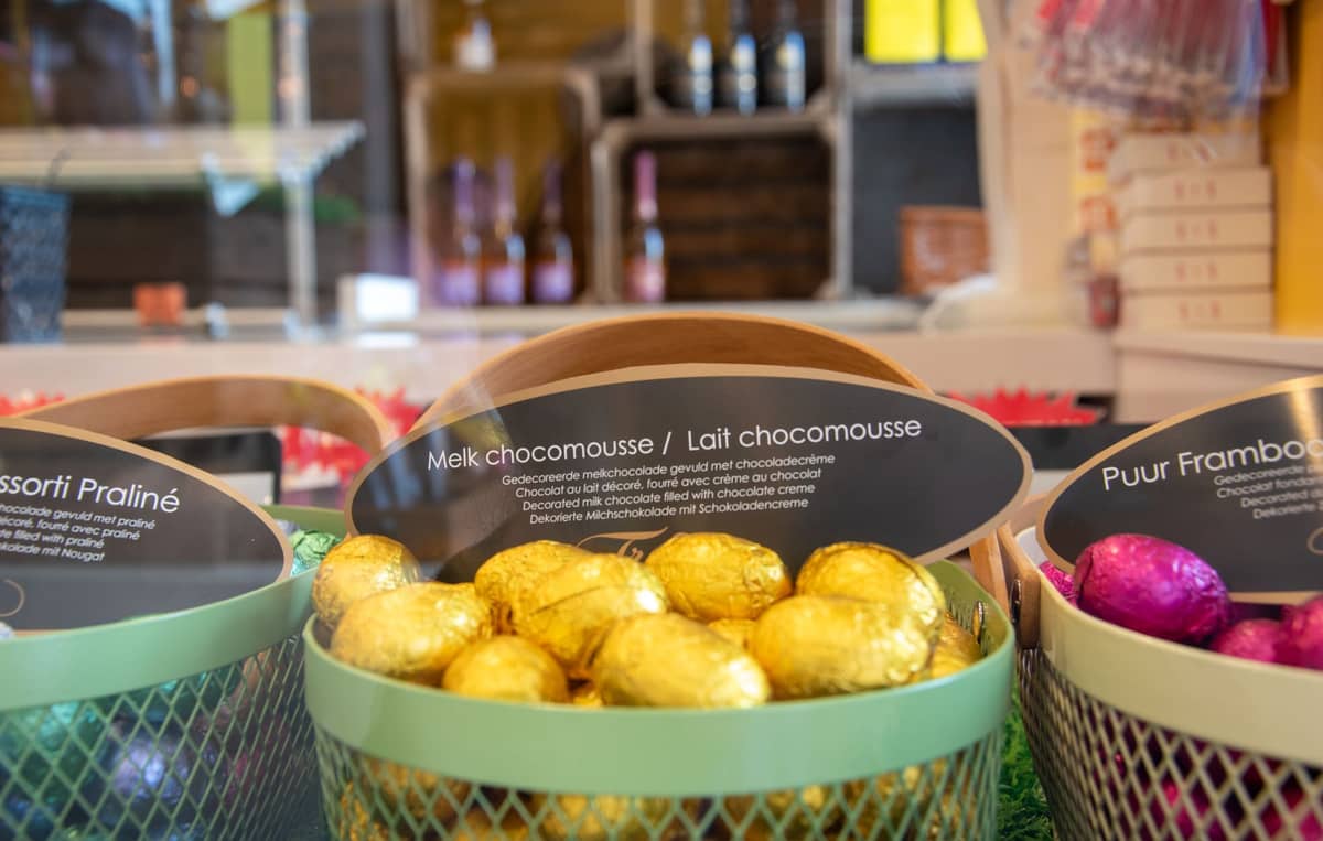 Exposição de ovos de chocolate belga sortidos numa chocolataria de Bruxelas com etiquetas em francês e neerlandês visíveis.