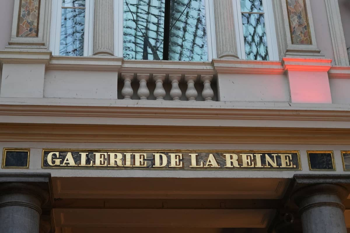 Placa de entrada da Galerie de la Reine com parte do teto de vidro e colunas de pedra visíveis.