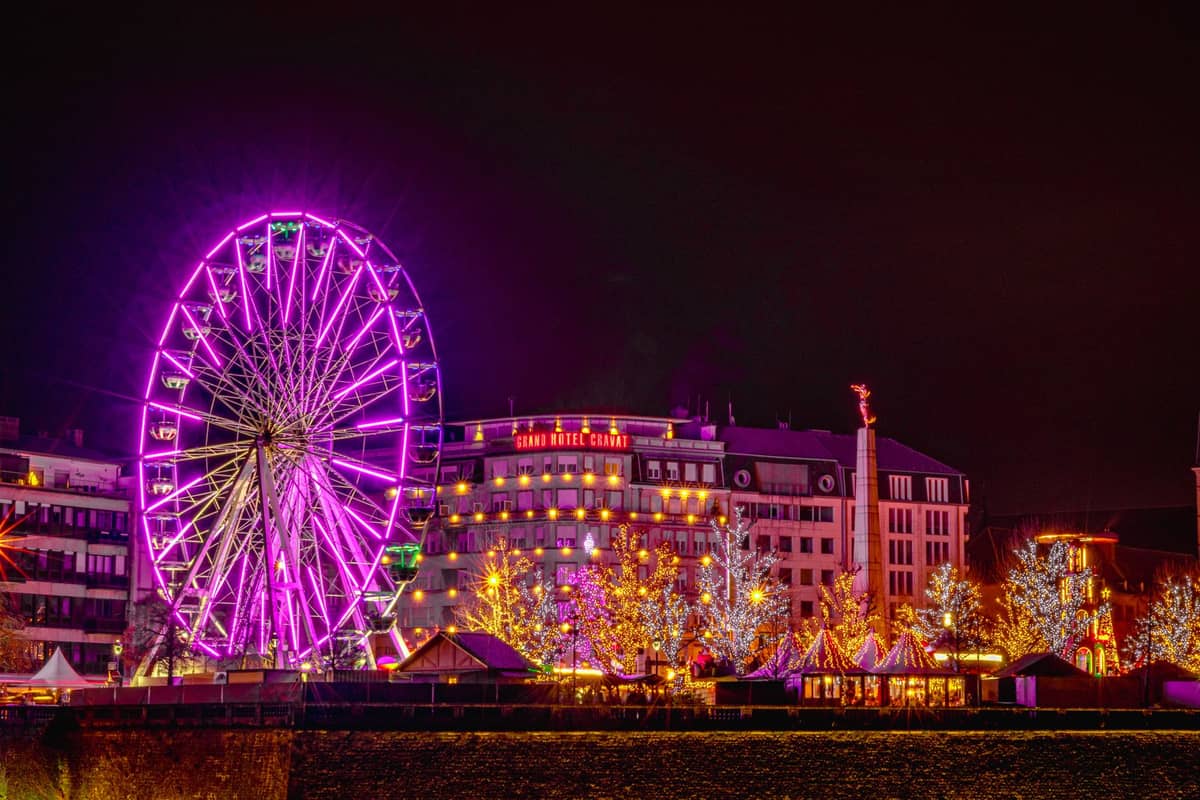 Mercado de Natal noturno em Bruxelas com uma grande roda-gigante iluminada e luzes festivas em edifícios e árvores.