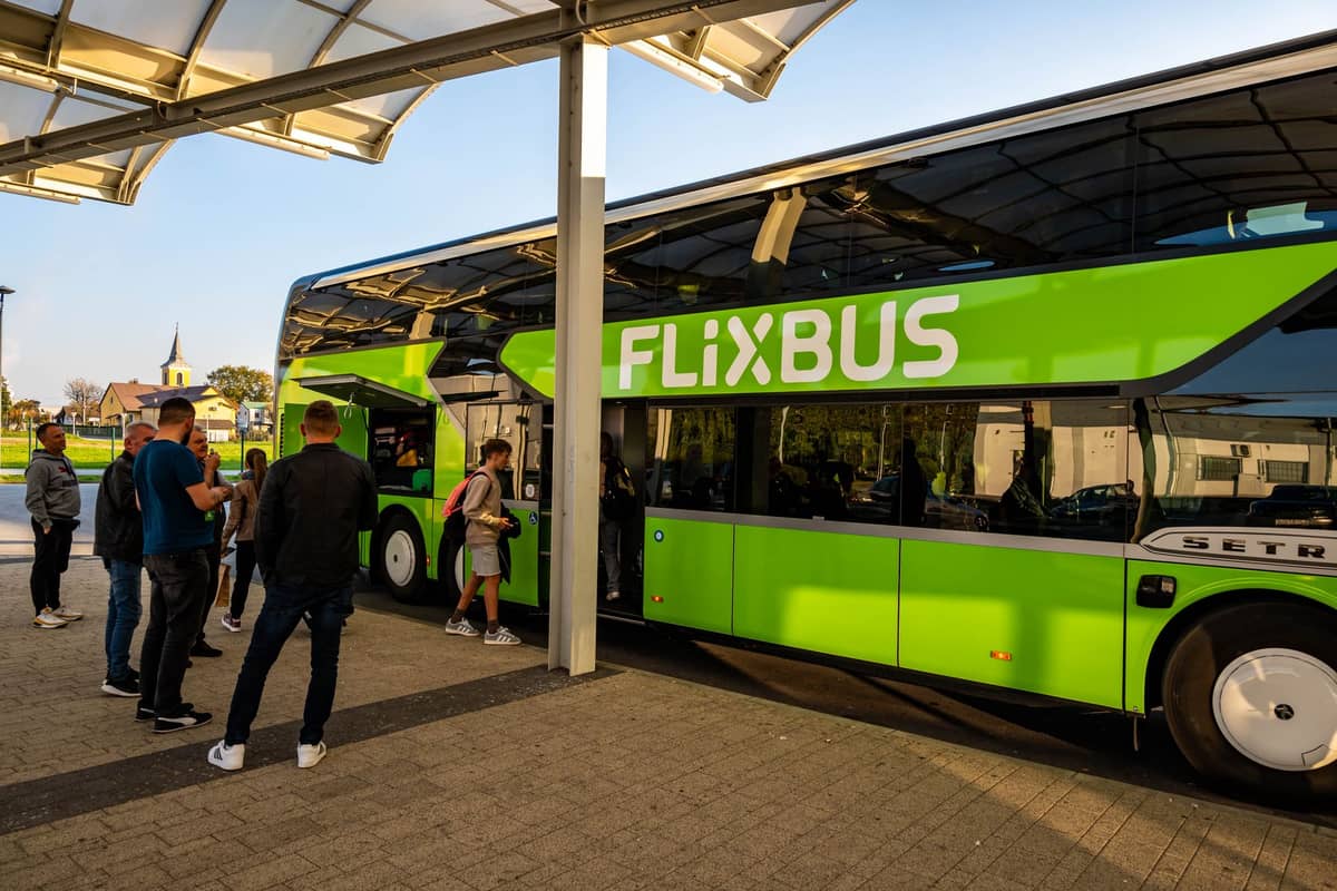 Pessoas embarcando em um ônibus de longa distância FlixBus em uma parada coberta com a identidade visual verde da FlixBus visível.