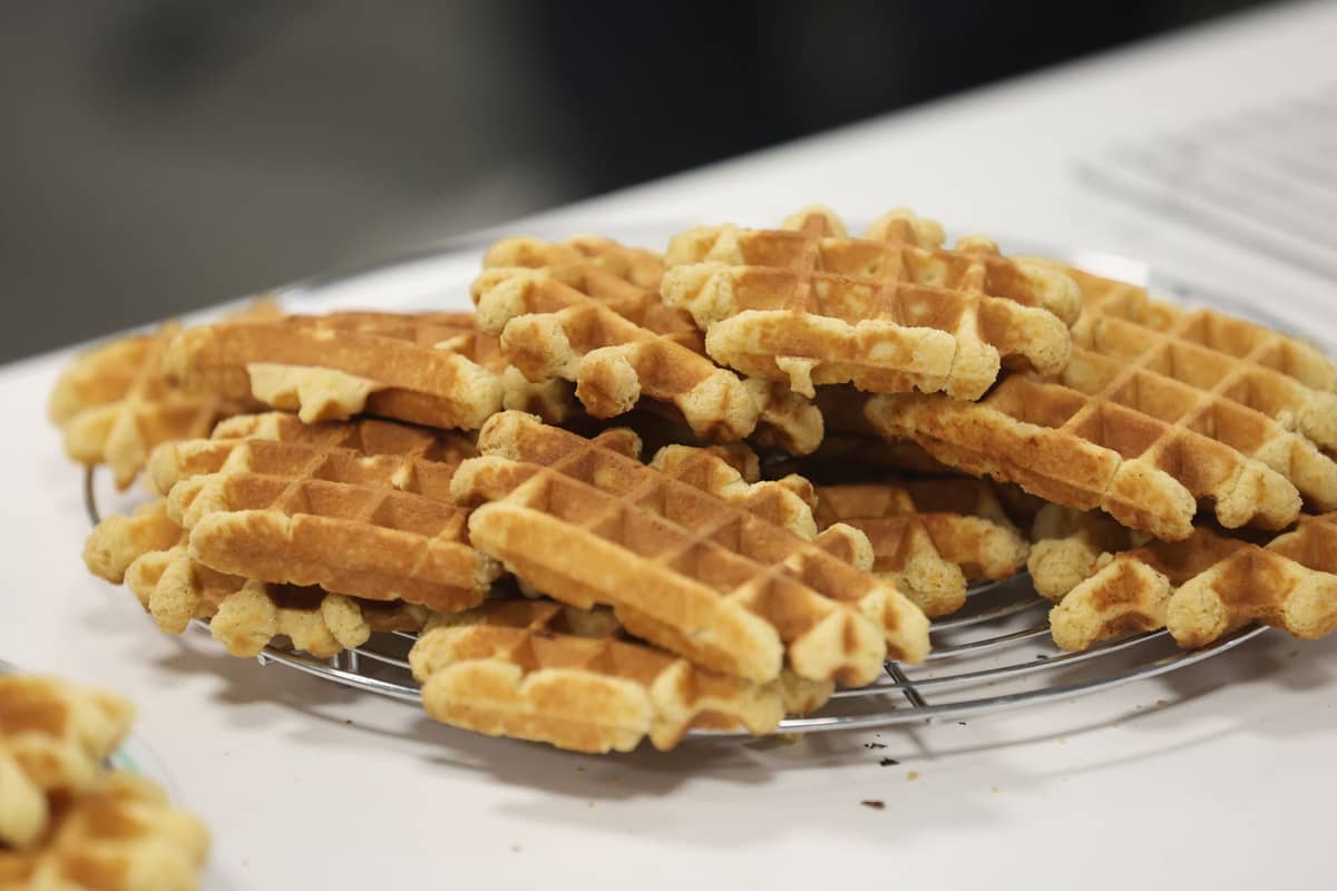 Vários waffles de Liège com sua característica forma irregular e grossa empilhados em uma grade de resfriamento sobre um balcão.
