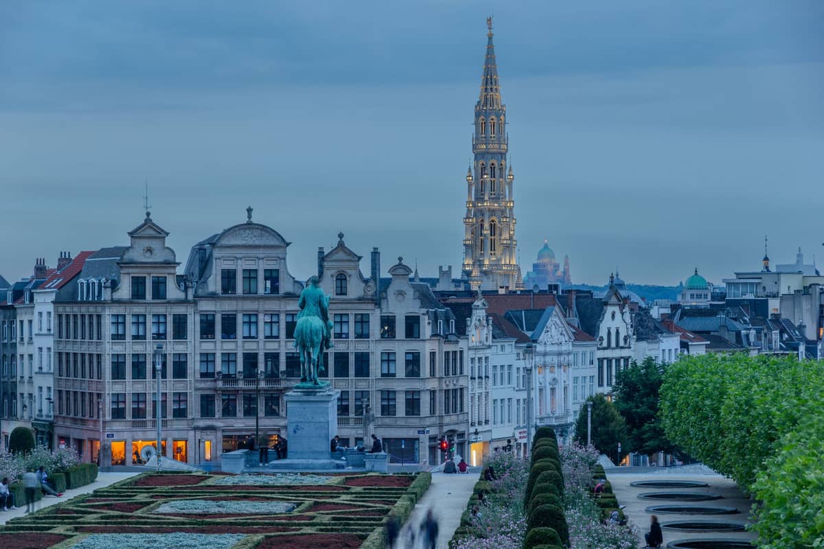 Vista do centro histórico de Bruxelas com um jardim, uma estátua, edifícios clássicos e a torre iluminada da Câmara Municipal de Bruxelas ao fundo