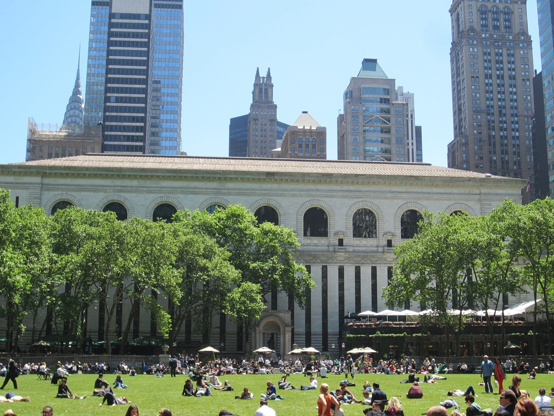 Bryant Park in una giornata di sole con persone che si rilassano sull'erba, circondato da alberi verdi e gli iconici grattacieli di Midtown Manhattan.