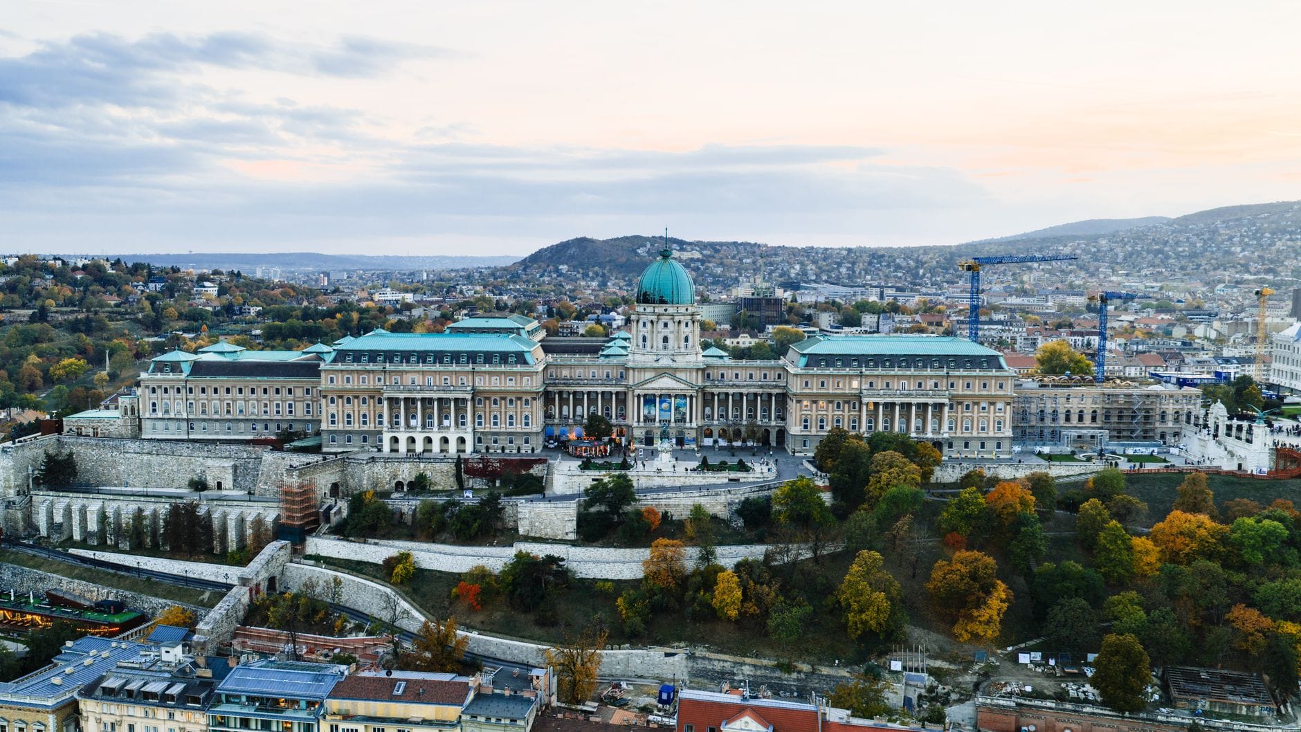 Vista aerea del Castello di Buda sul Colle del Castello, con il grande palazzo a cupola, i giardini e il panorama di Budapest al tramonto.